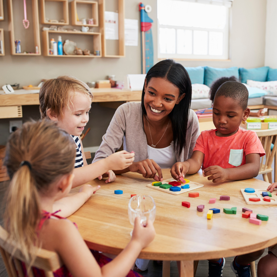 A Black woman teacher working with pre-school students at a table using manipulatives.