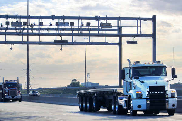 White Flatbed Truck driving Under 407 ETR Gantry with Dump Truck Behind