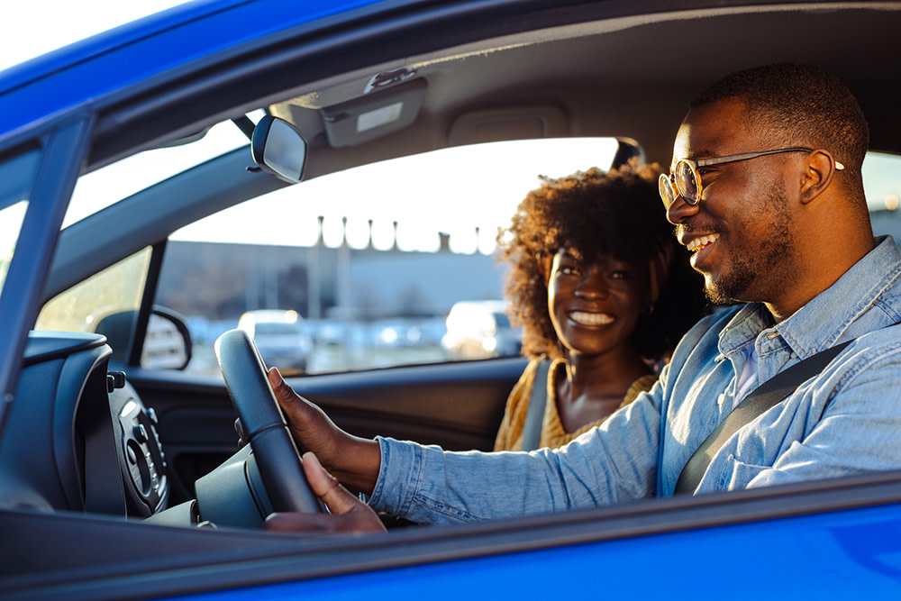 A man and a woman sitting in the front seat of a blue car