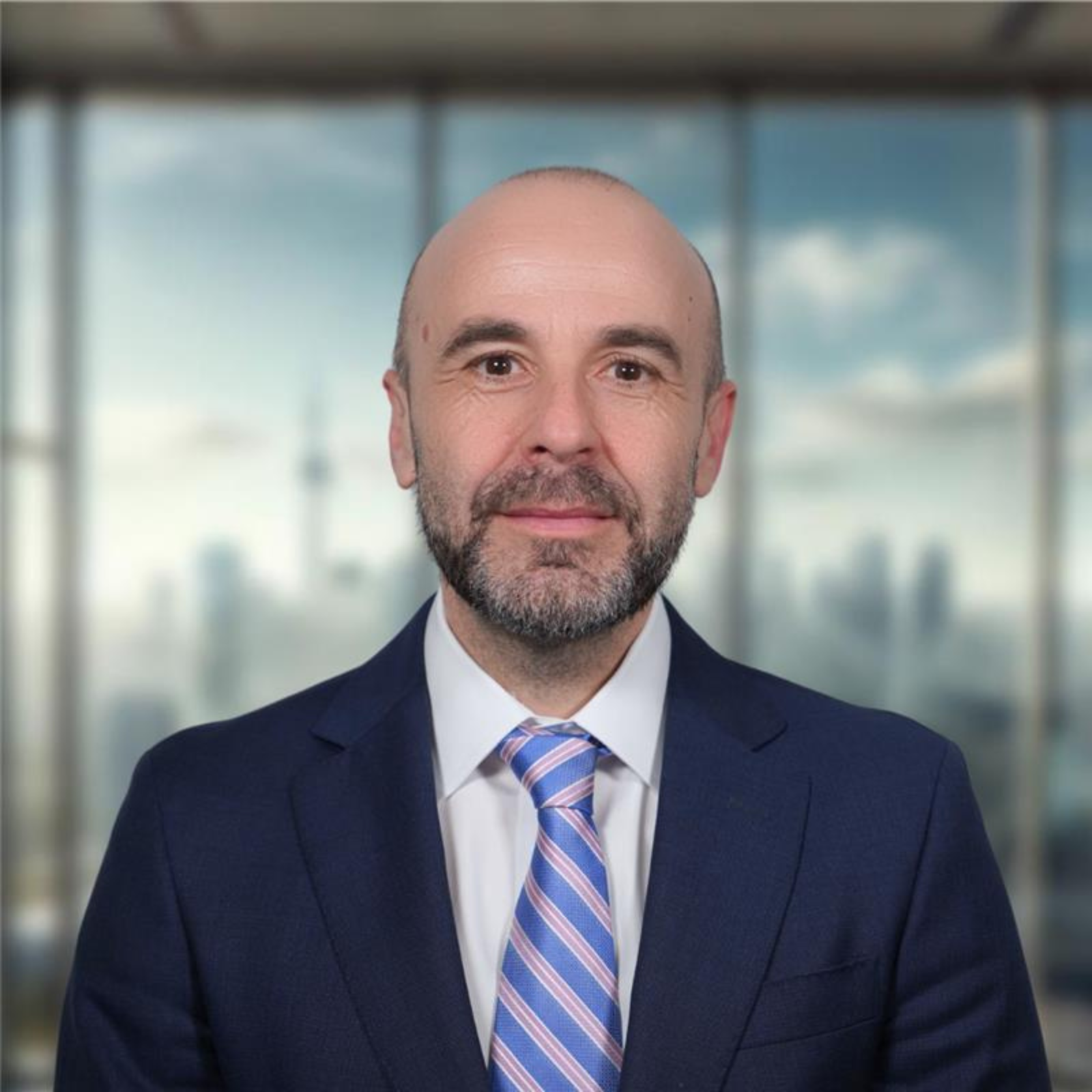A man with short, brown hair wearing a navy blue blazer, white shirt, and blue tie.