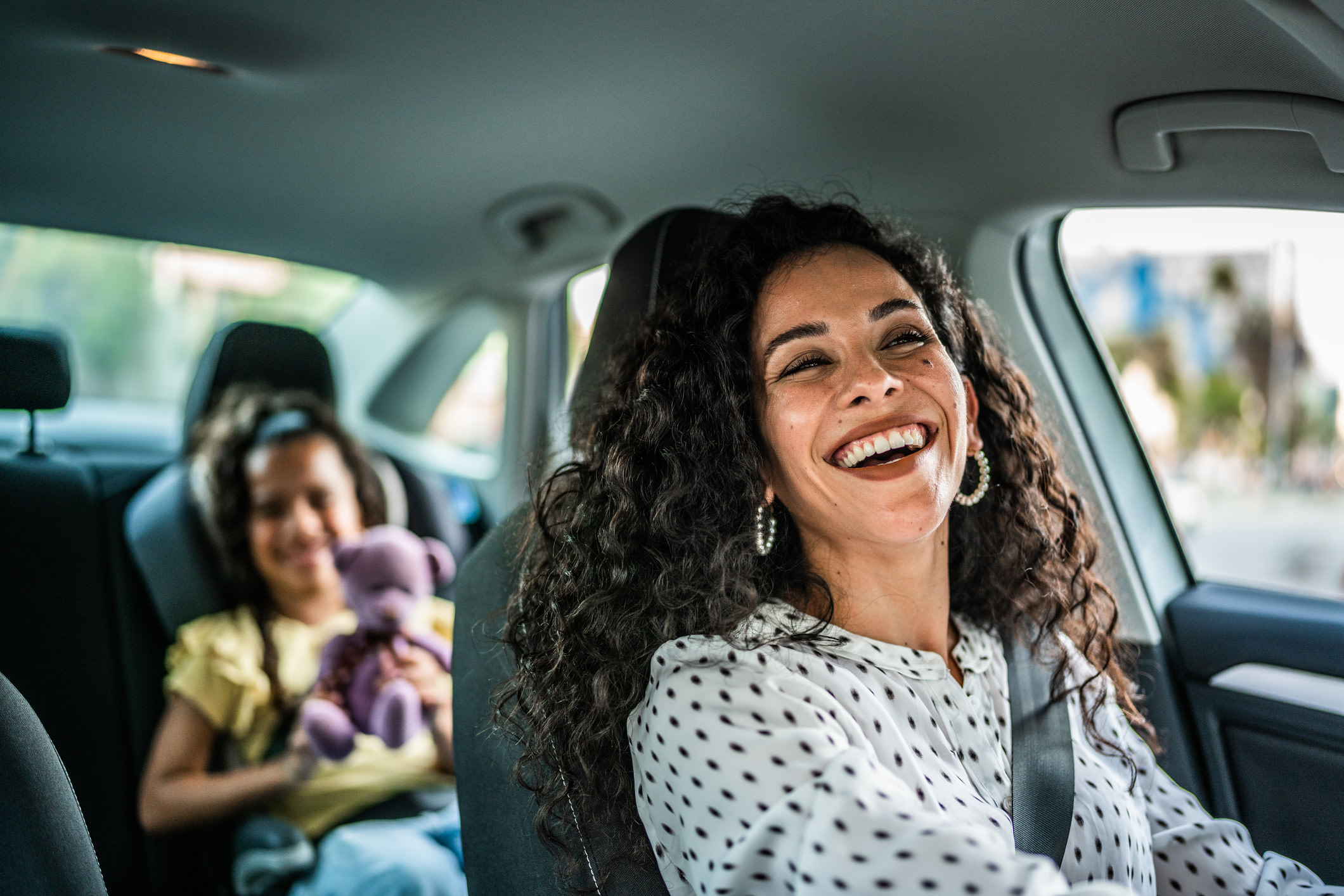 Woman driving with daughter in the back seat both smiling