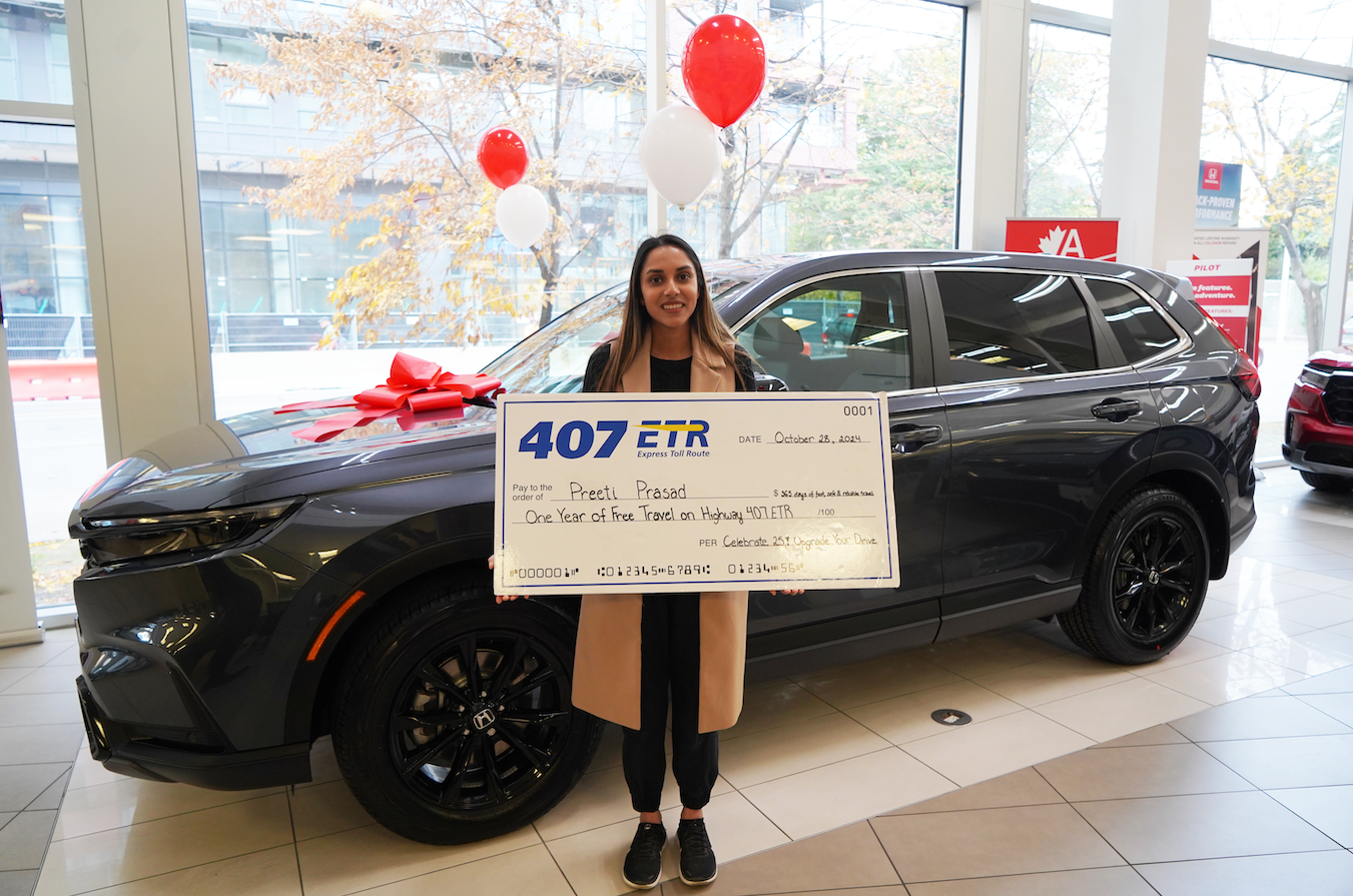 A woman standing in front of a 2025 Honda CR-V Hybrid holding a giant cheque for a year of free travel on Highway 407 ETR