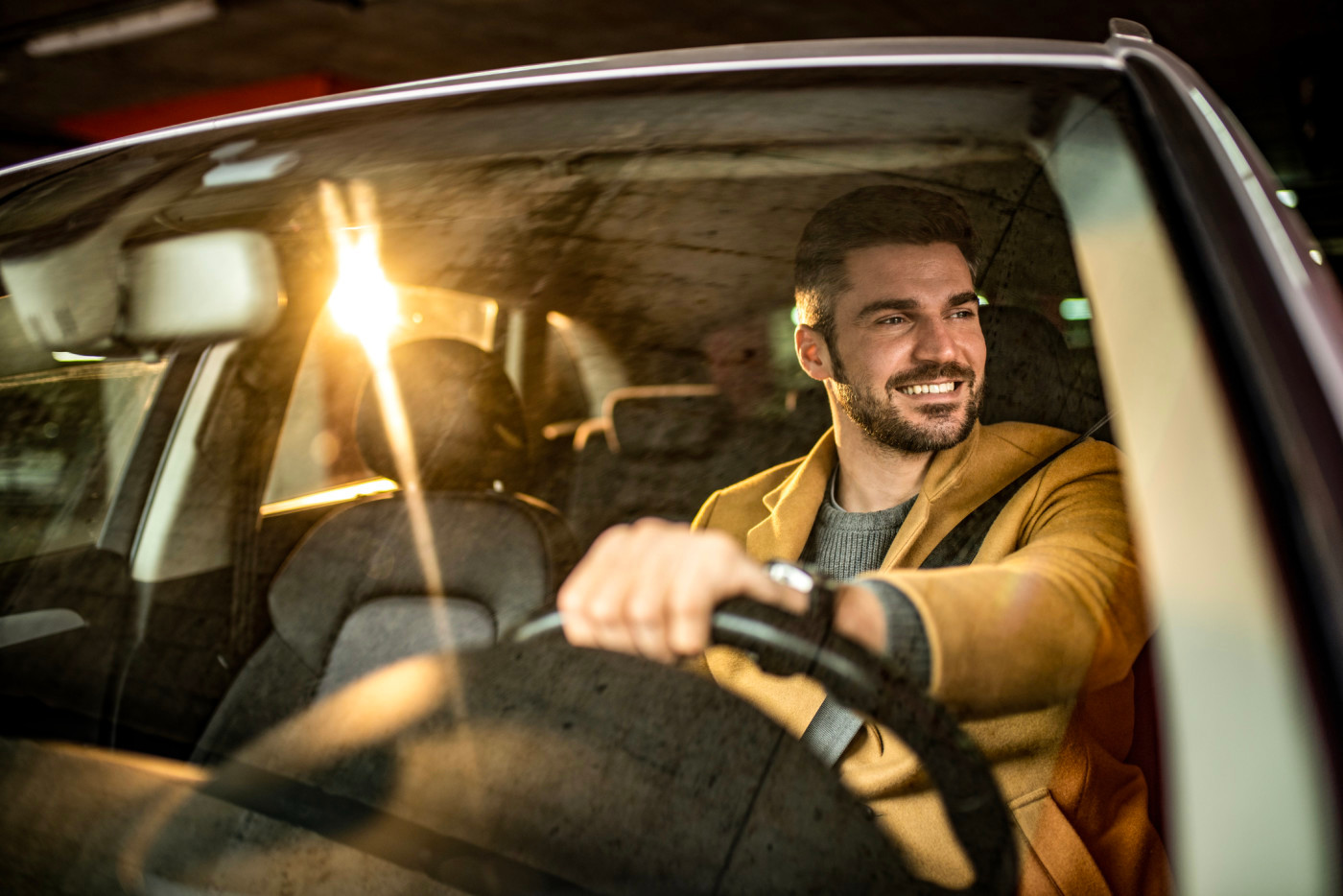 A man driving in a car with the sun behind him.