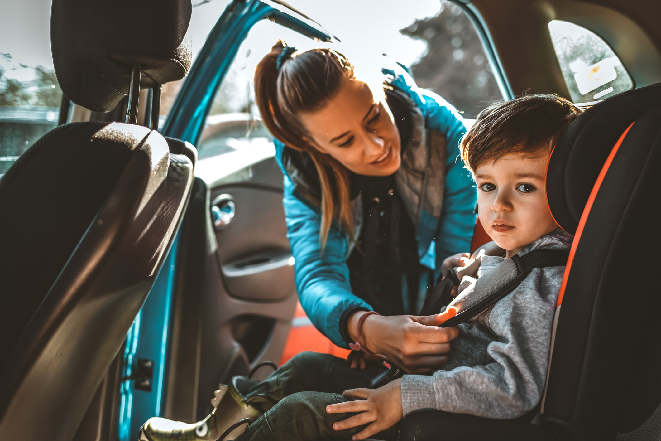 A woman buckling her son into a car seat.