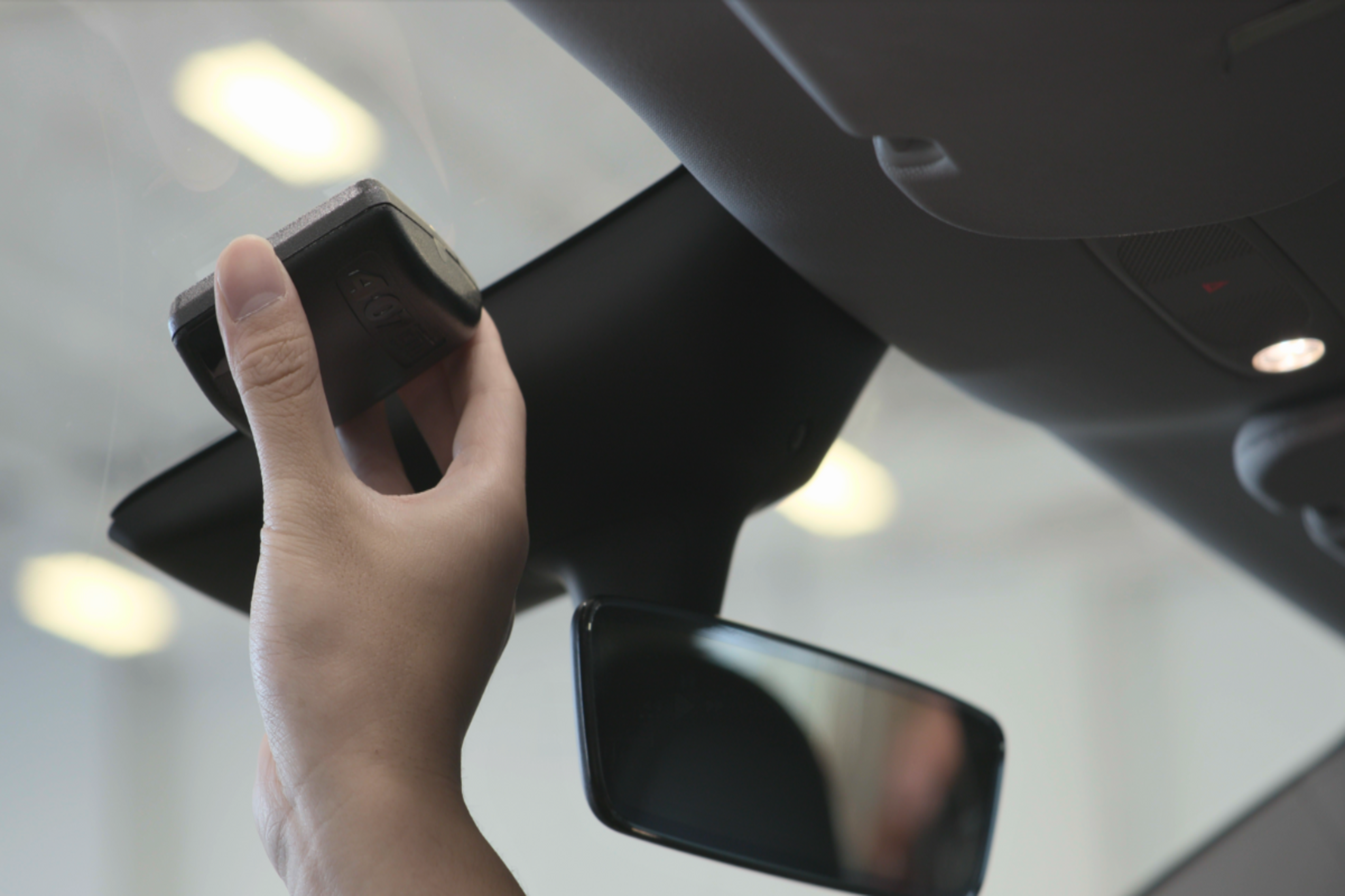 closeup of someone installing their 407 ETR transponder to the left of their rearview mirror