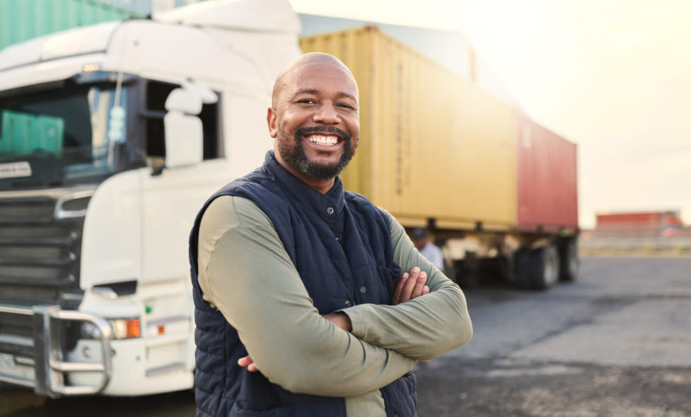 A man with his arms crossed, smiling while standing in front of a truck.