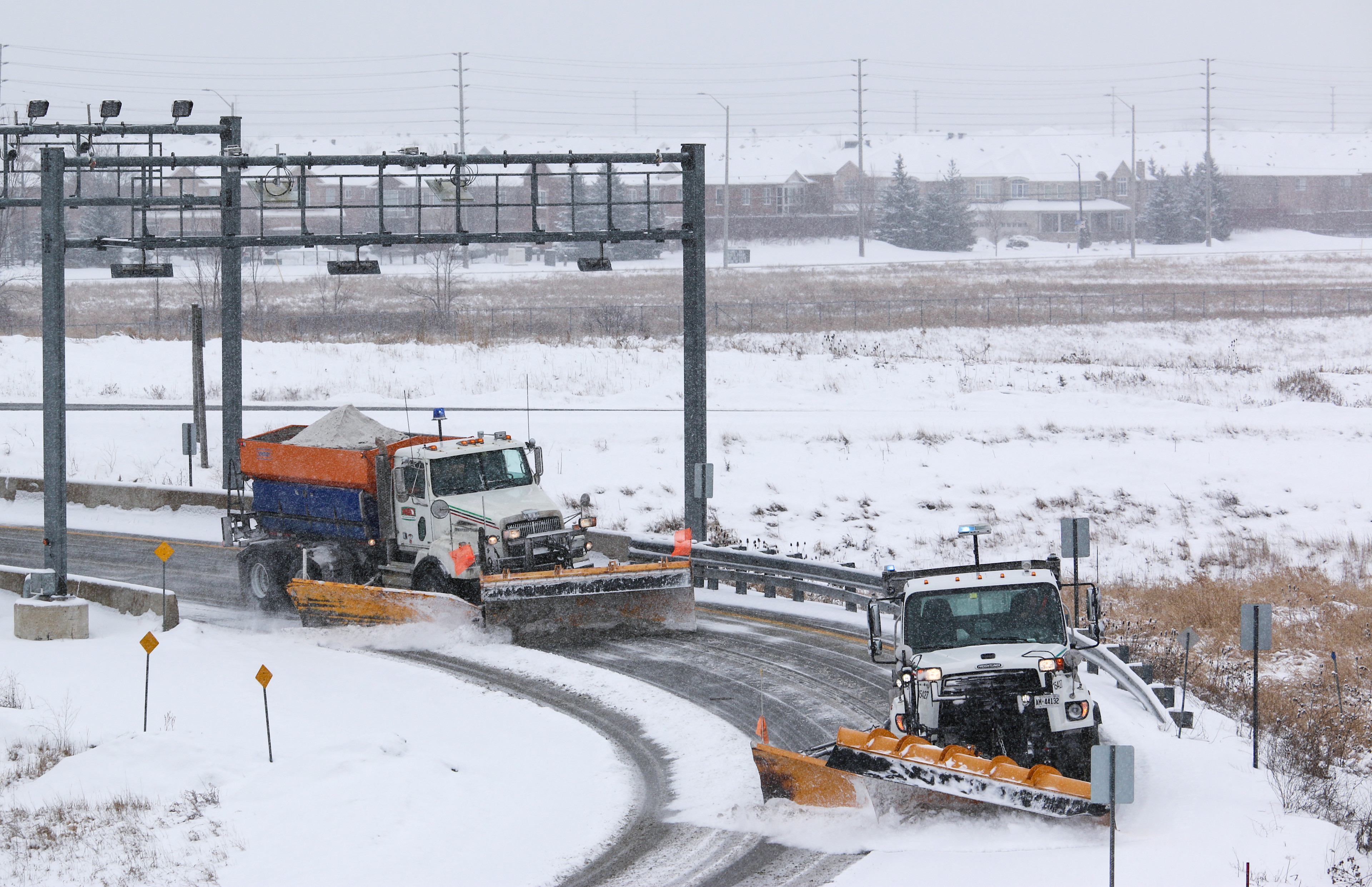 Two snow plows driving under a gantry on Highway 407 ETR.