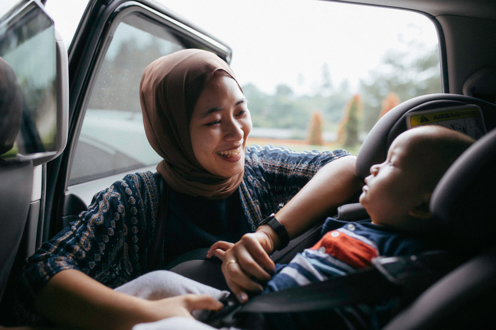 A woman strapping a baby into a car seat while smiling.