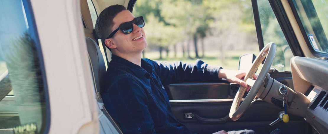 Man with sunglasses sitting in driver's seat of vehicle smiling