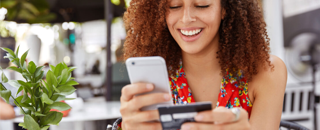 woman sitting next to plant, smiling holding phone and credit card