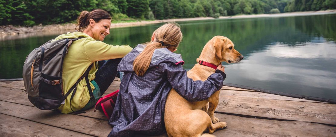 two women smiling sitting on a dock with cute dog