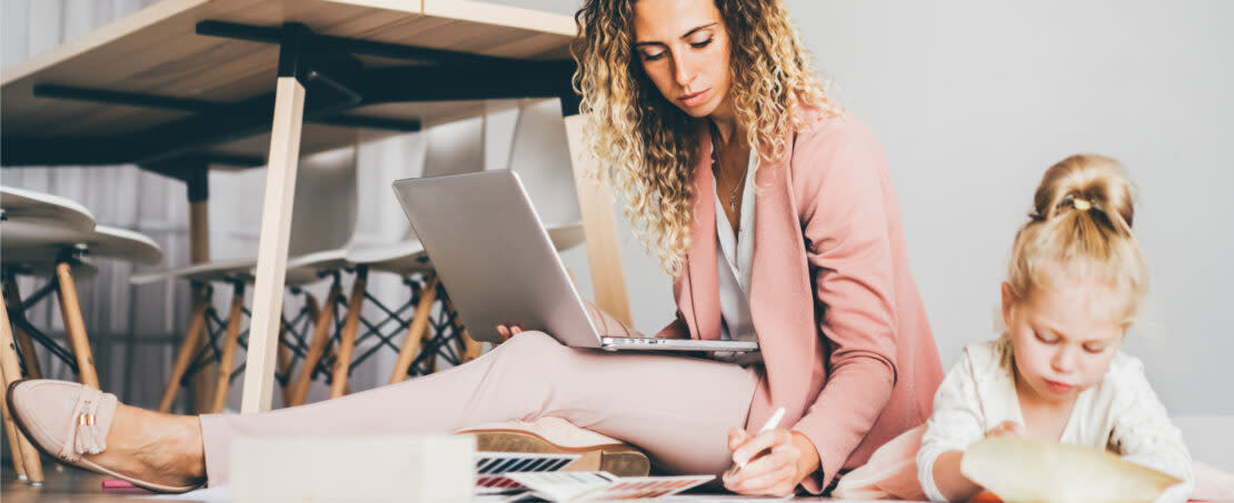 Woman in pink blazer sitting on ground with laptop in lap next to young girl looking at documents