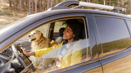 happy, smiling young woman driving car window rolled down with her dog in passenger seat