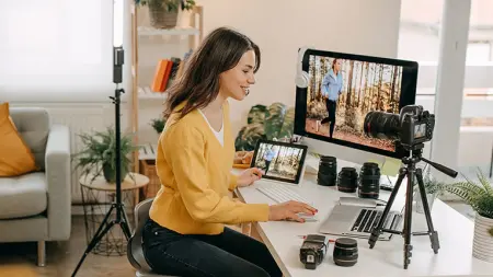 Woman working from her living room desk using camera equipment hooked up to her laptop and iPad.