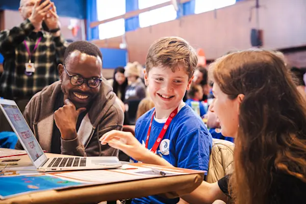 A smiling young person shows his tech creation to two volunteers at a Coolest Projects event.