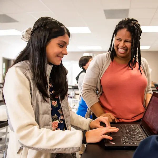 A smiling student and teacher at a laptop.