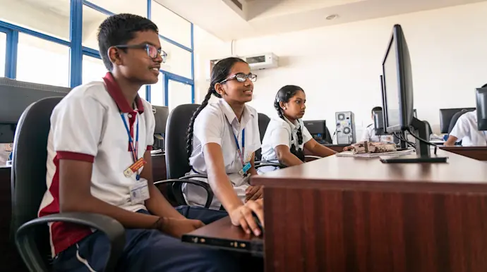 Three young people at desktop computers in a classroom in Chennai, India.