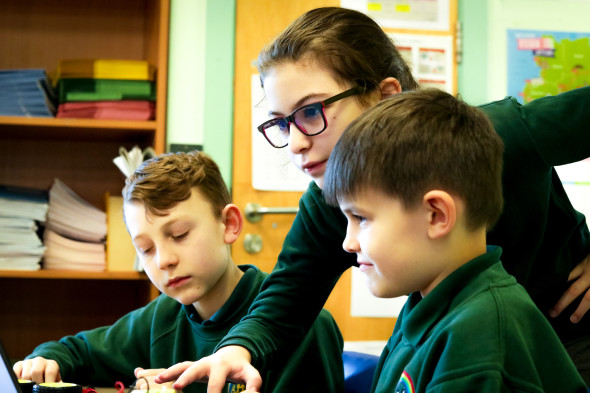 An older student helps two younger students with their computing project