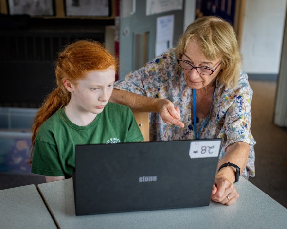A girl and a female educator work at a laptop together.