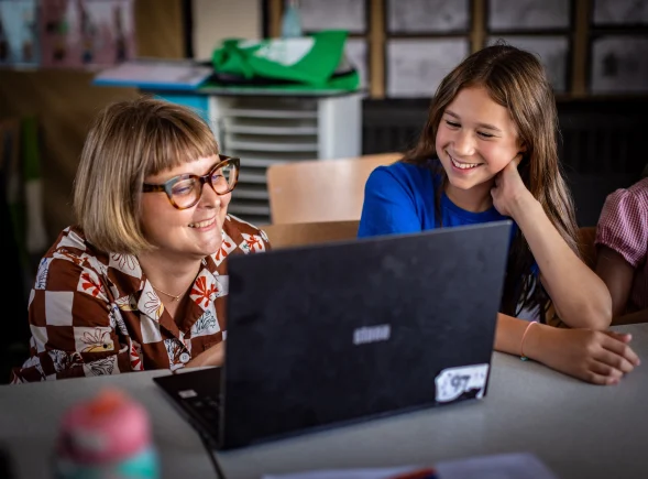 A young person and an educator smile at a laptop at a Code Club session.