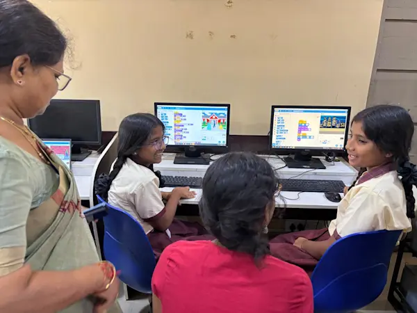 Two children working at computers supported by teachers. 