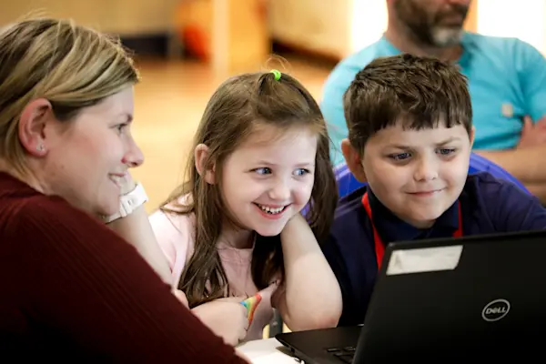Two young people and a mentor smile at a laptop in a coding club session.