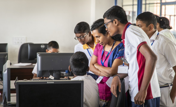 A teacher and a group of students gathered around a computer