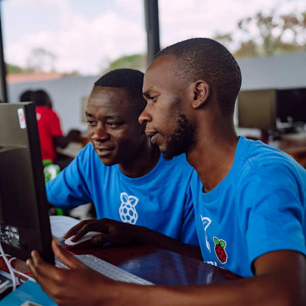 Two men learn at a computer in a Kenya classroom.