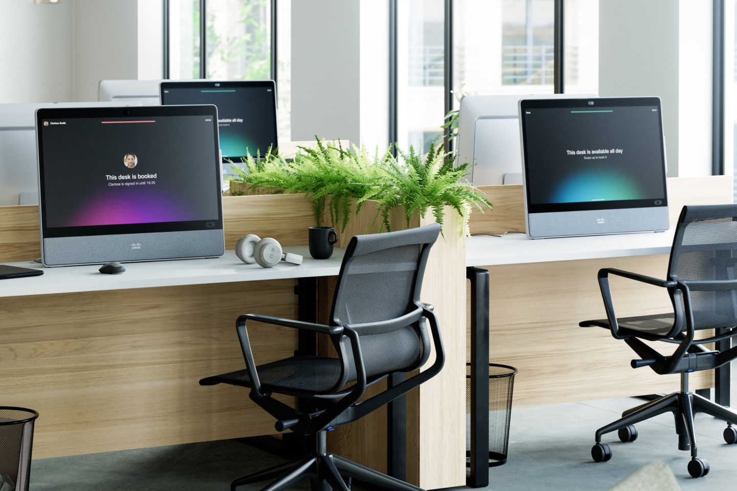 Office space containing multiple desks with Webex DeskPros. Some display w/ red-ish details stating desk is booked, others that the desk is available all day with green details in the ui