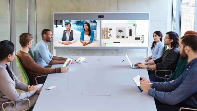 7 people around a conference table in a video meeting with a two other people through a Cisco Webex Room 70 Dual G2