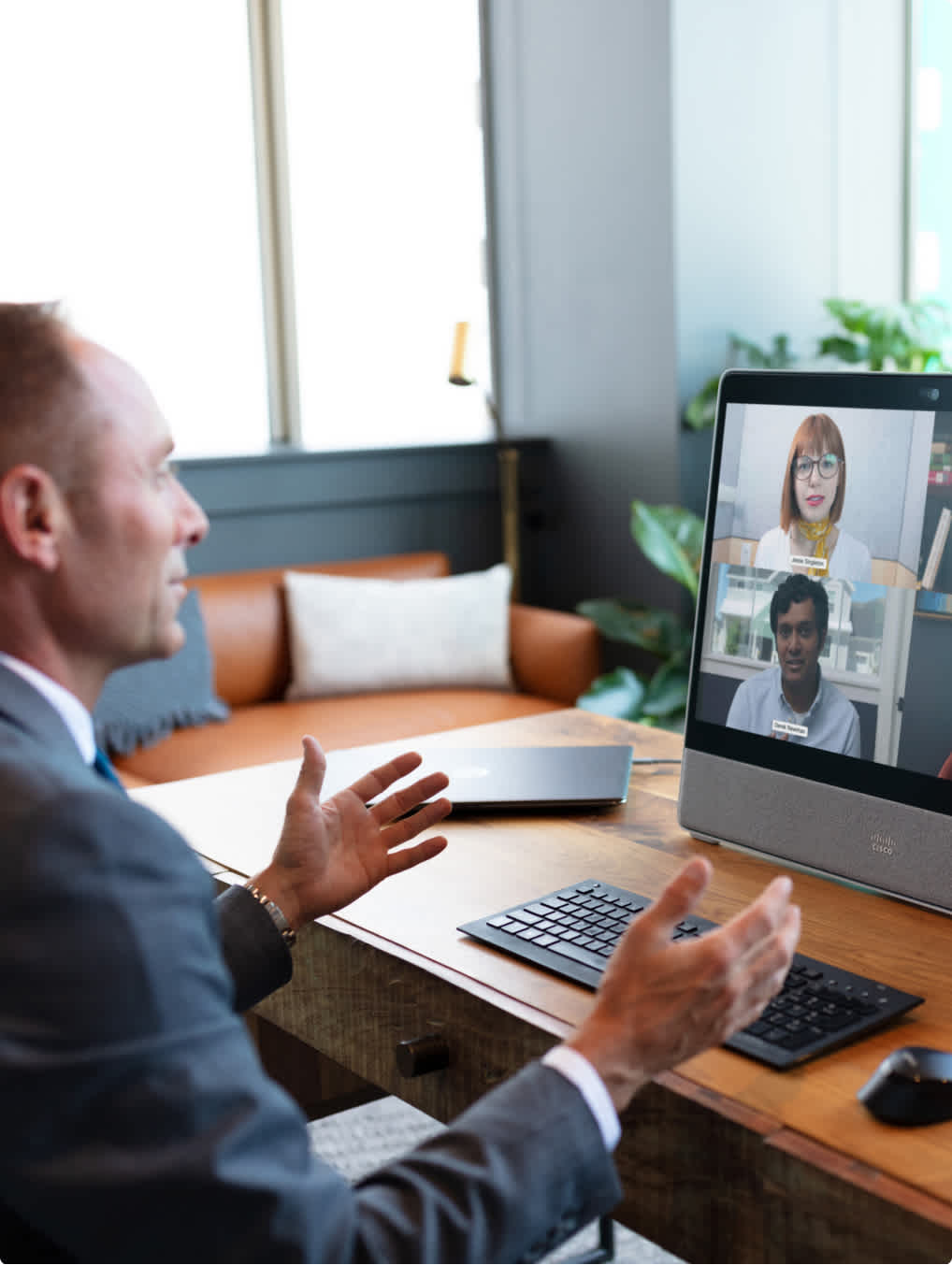 Man in front of a Webex Desk gesticulating while in a video call.