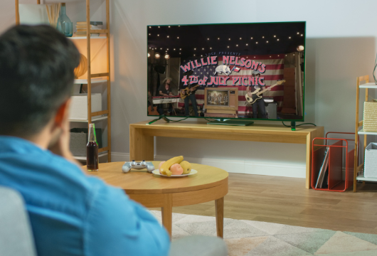 Man watching Willie Nelson's 4th of July Picnic Live Stream video on his living room TV.