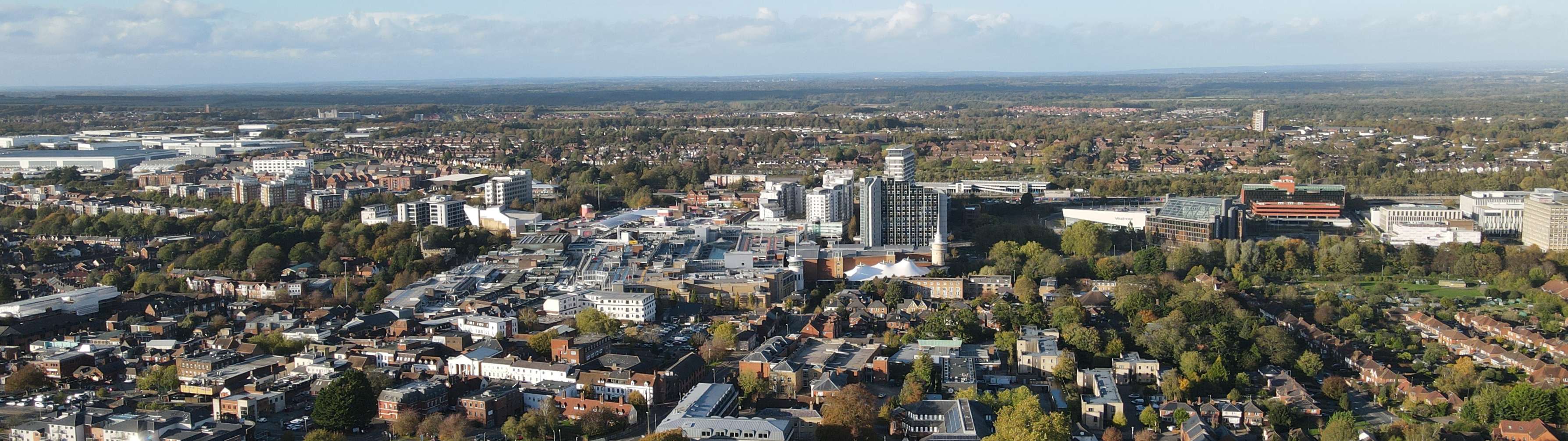 Tall office buildings dominate the skyline of Basingstoke, surrounded by the greenery of parks and trees.