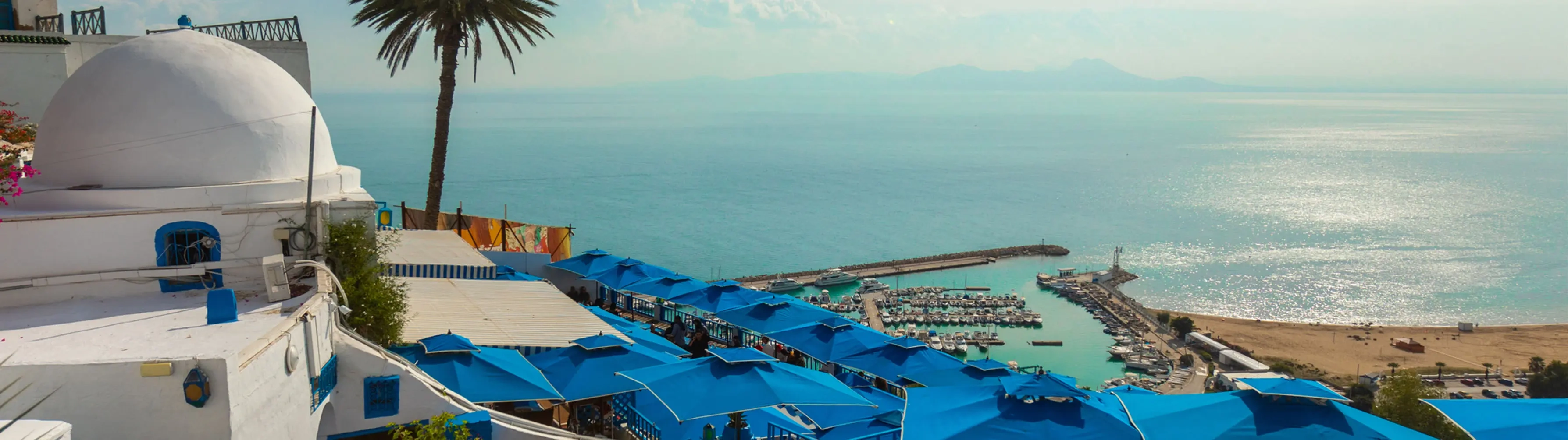 The sparkling Mediterranean from the hillside of Tunis, with blue parasols in the middleground.