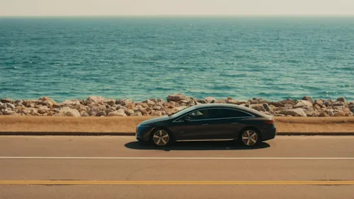 Side shot of a Blacklane Mercedes EQE driving along a coastal road with the ocean stretching behind it.