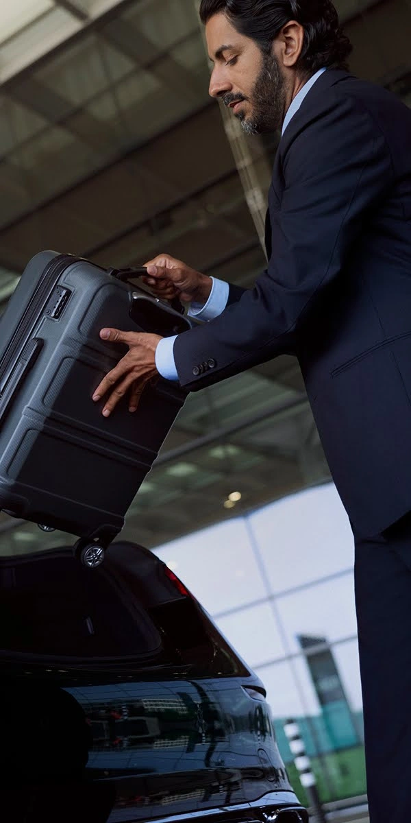 A Blacklane chauffeur takes a suitcase out of the trunk of a black Mercedes limousine.