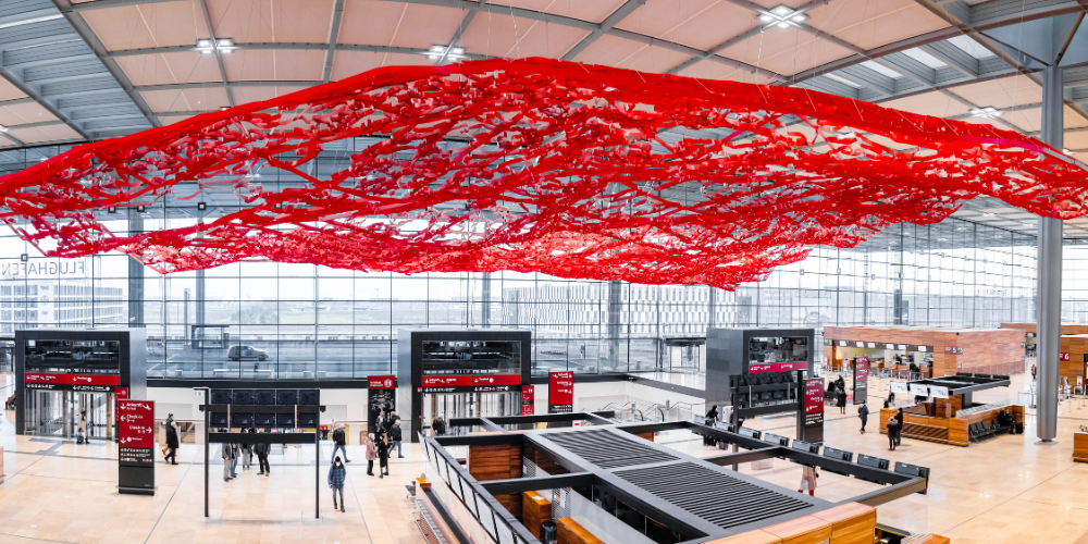 The magic red carpet, a large red metal mesh sculpture, hangs and flutters in the check-in hall of Berlin Brandenburg Airport.