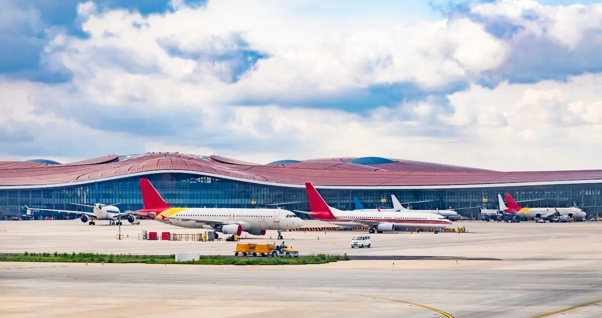 Planes taxiing on the flight apron of Beijing Daxing Airport with the terminal building in the background.