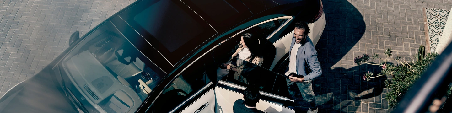 A businessman and businesswoman get into a chauffeured Blacklane Mercedes EQE limo.