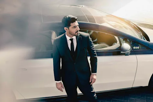 ドバイでスマートな服装の運転手が車の近くに立っている。