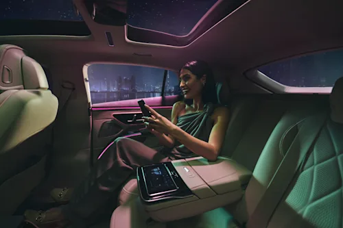 Una mujer sentada en el asiento trasero del Mercedes EQS sonríe a su teléfono por la noche.