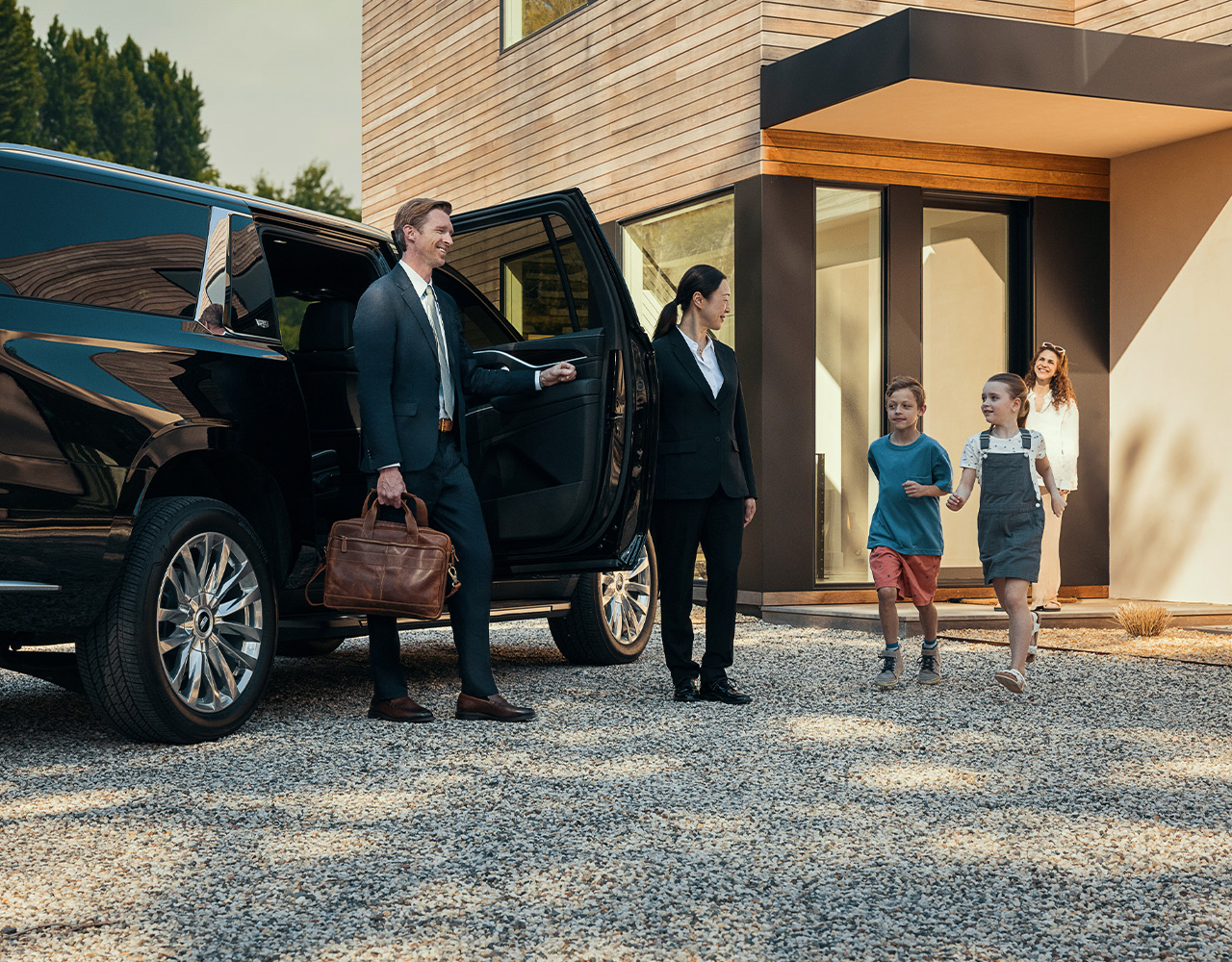As a chauffeur opens the door, a man leaves his car to be greeted by his waiting children.
