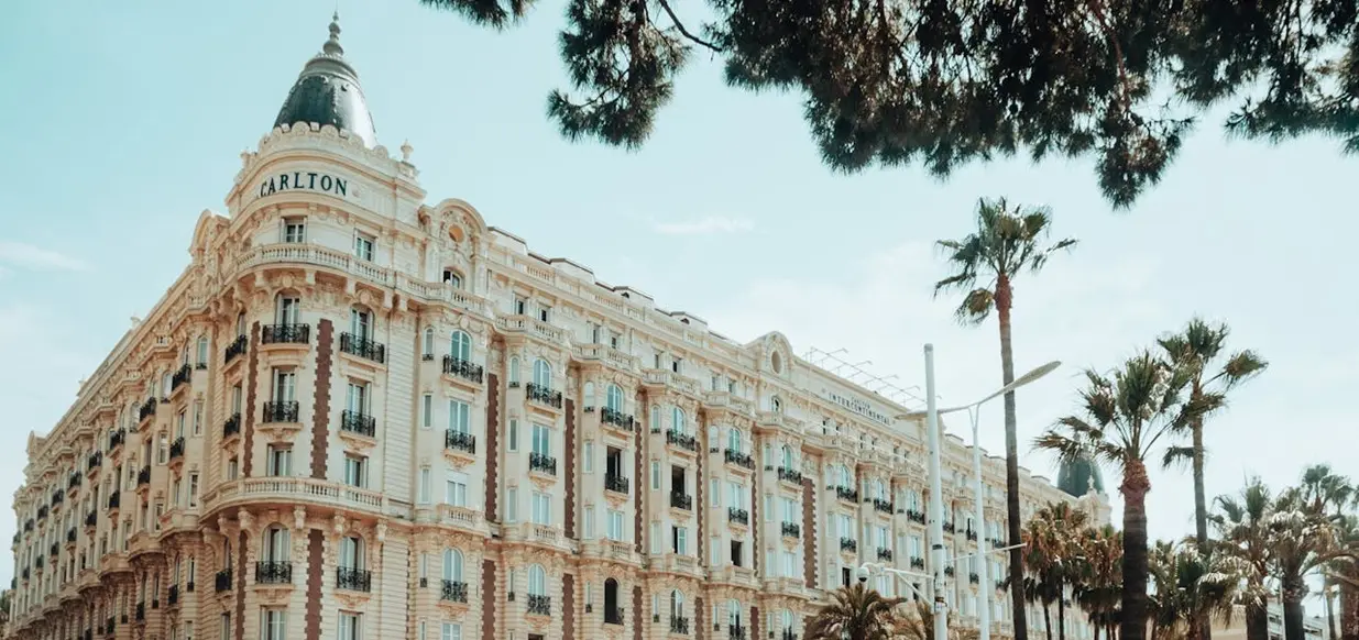 Exterior shot of the upper floors of the Carlton Cannes hotel in the South of France, during daylight with trees in the foreground.
