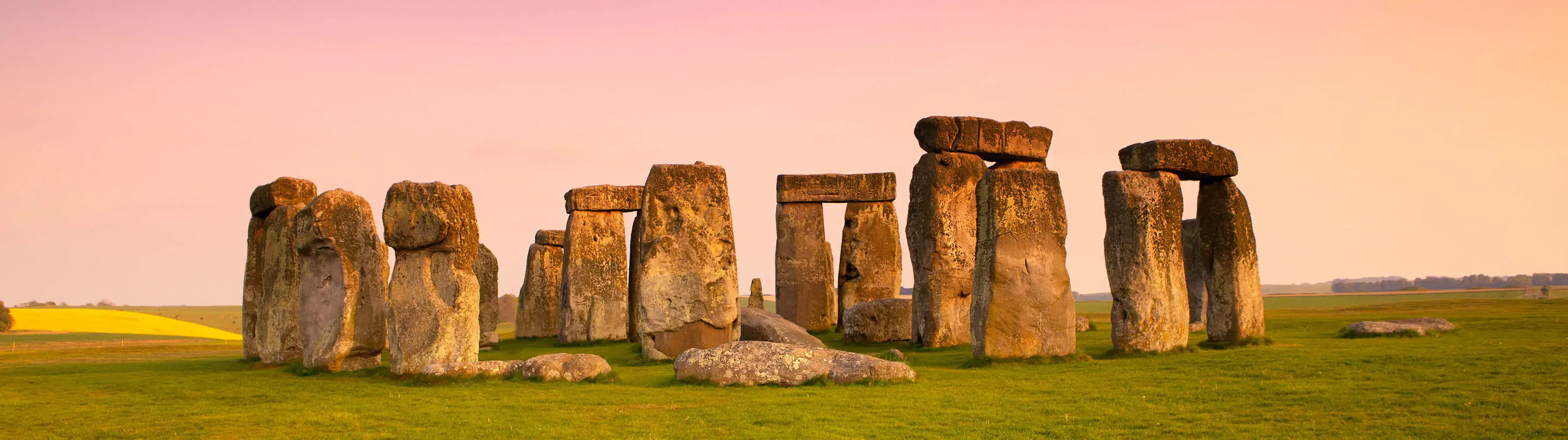 An image of the ancient stones of Stonehenge with a pink dawn sky in the background.