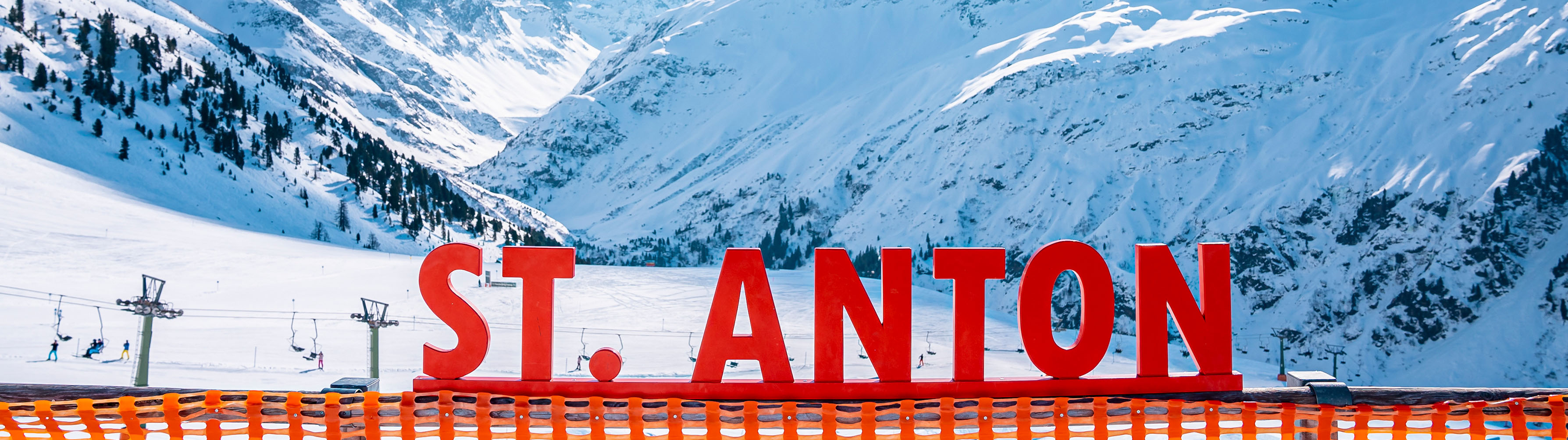 The fresh snow of St. Anton lies in the background with the name of the village in the form of a huge red sign dominating the foreground.