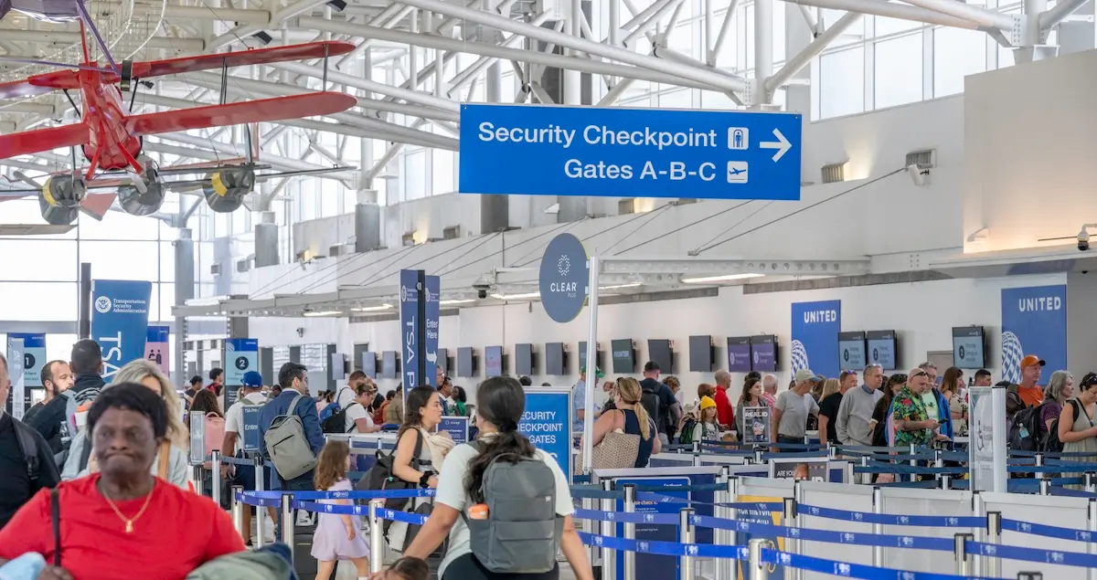 Security checkpoints at Fort Lauderdale Airport, showing busy crowds, check-in desks, and a red model plane hung from the ceiling.