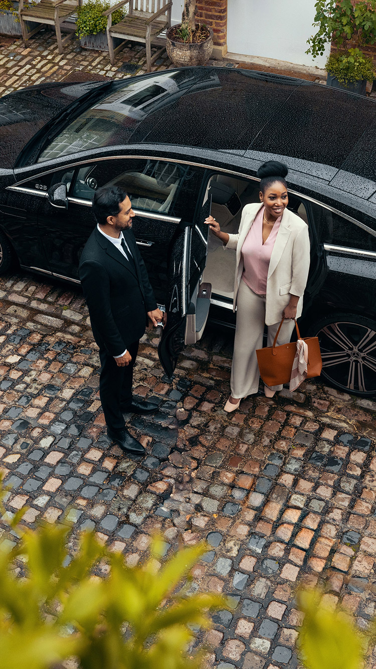 A Blacklane guest steps out of a black car with her chauffeur holding the door open.
