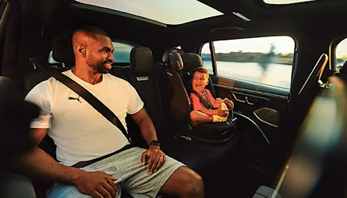 A man sitting in the backseat of a Mercedes EQS with his young child buckled into a car seat next to him.