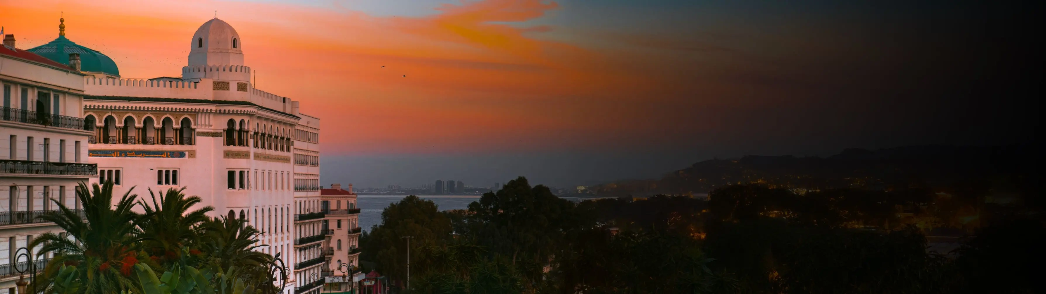 The Great Mosque of Algiers shot in front of an orange sunset, with the bay in the background.