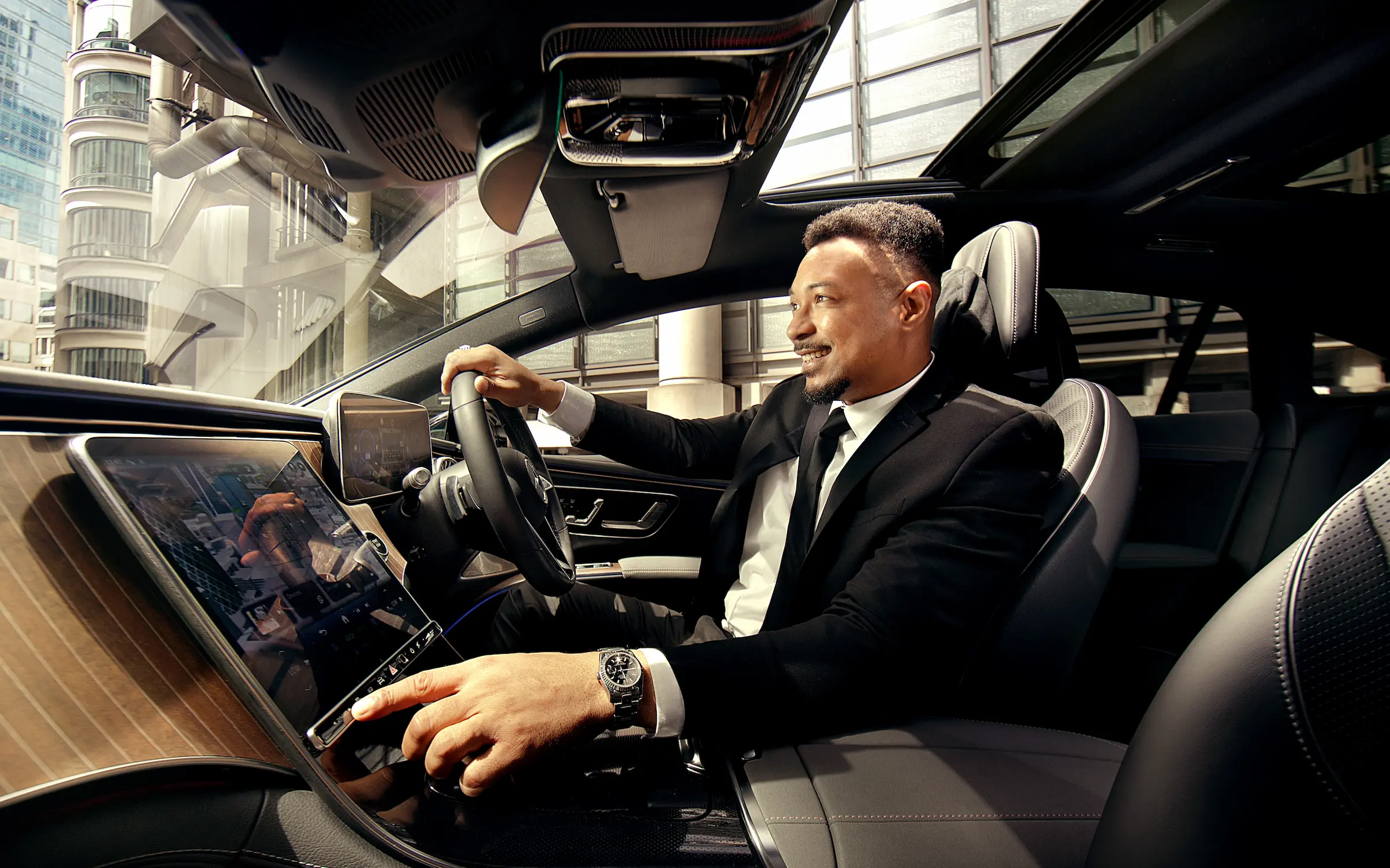 A Blacklane chauffeur smiles and adjusts a control while driving a Mercedes EQS.